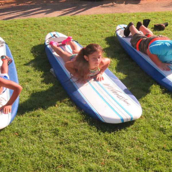 three kids practice getting up on a surfboard on dry land