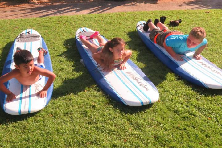 three kids practice getting up on a surfboard on dry land
