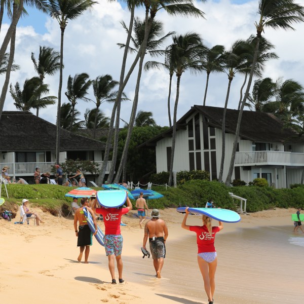 couple walking on the beach carrying surfboards on their heads