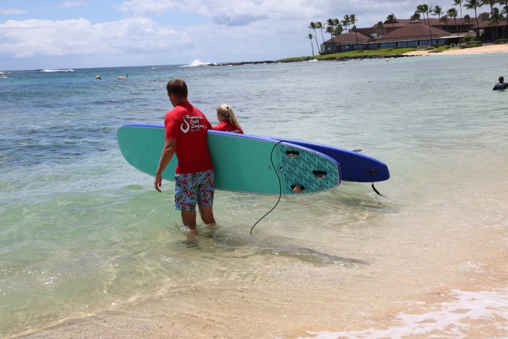 man and woman walking into water with surfboards