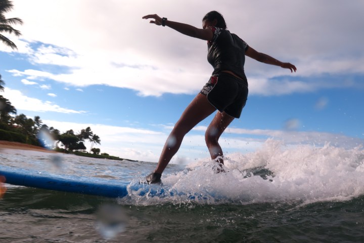 girl leaning back on her surfboard as she reaches shore