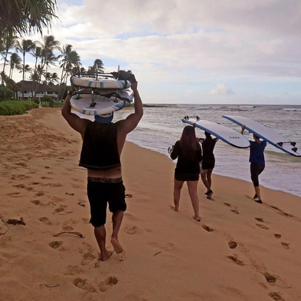 group walking on the beach holding surfboards on their heads