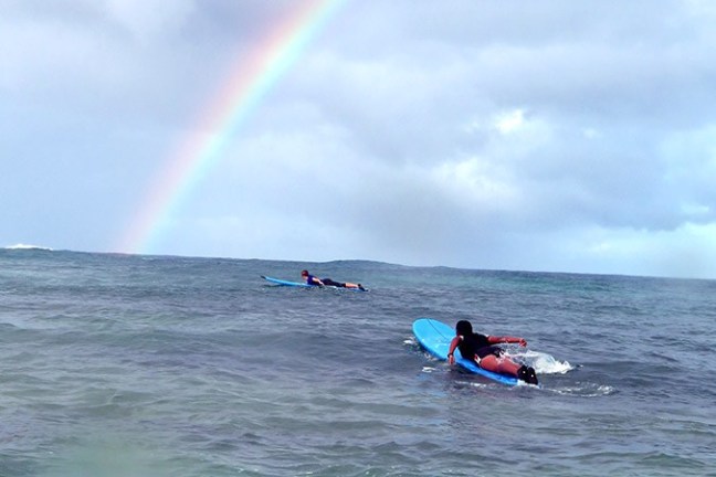 surfers paddling out under a kauai rainbow