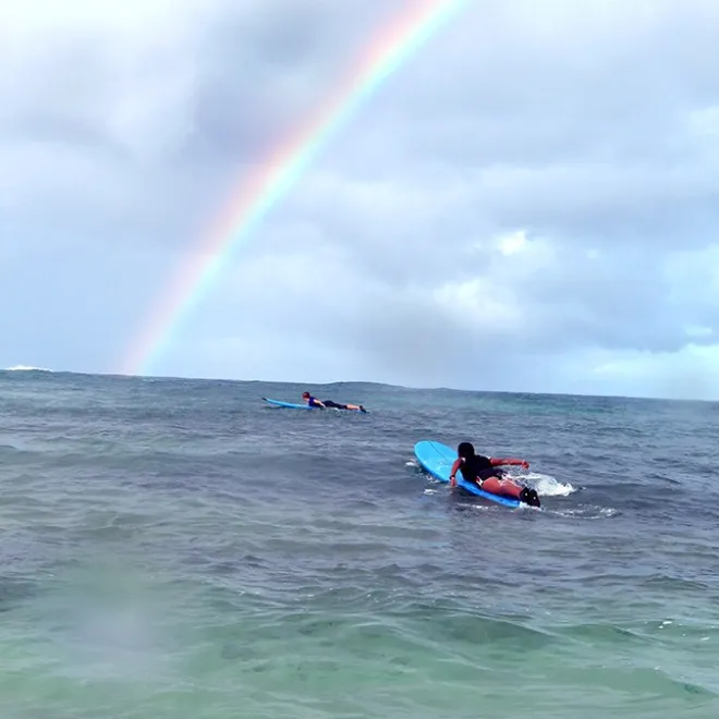 surfers paddling out under a kauai rainbow